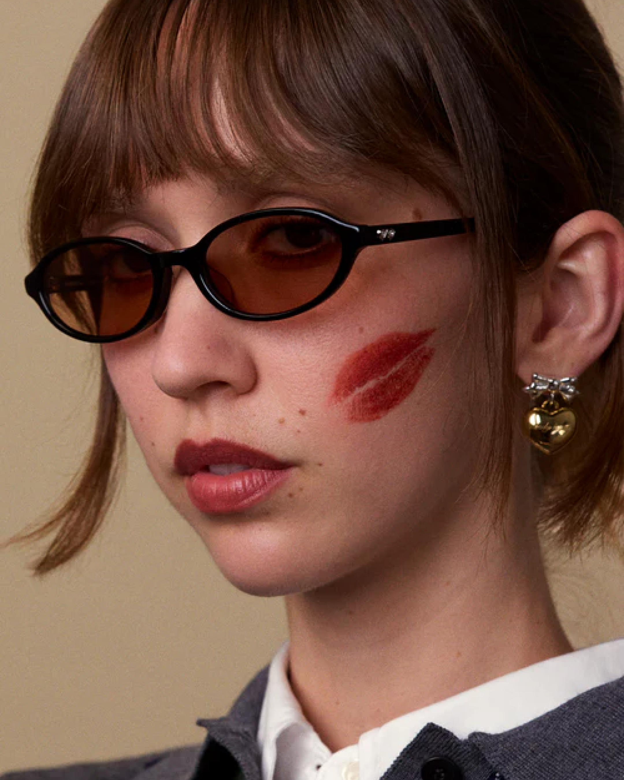 Model wearing Bonnie Clyde Baby sunglasses with black oval frames and brown-tinted lenses, close-up portrait